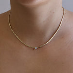 Gold necklace with a diamond on a person's neck against a neutral background