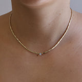 Gold necklace with a diamond on a person's neck against a neutral background