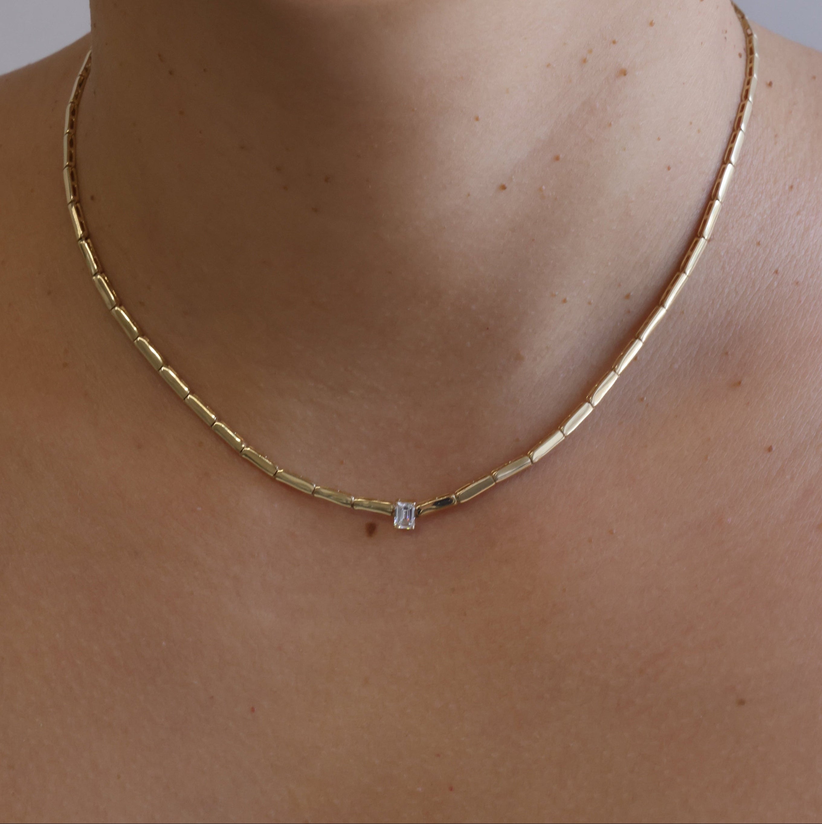 Gold necklace with a diamond on a person's neck against a neutral background